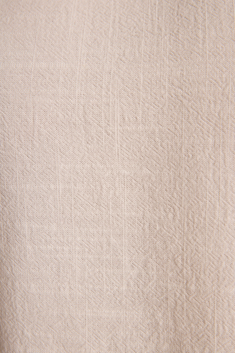 Detail of woven cream linen fabric with subtle geometric texture, linen resort wear for women.