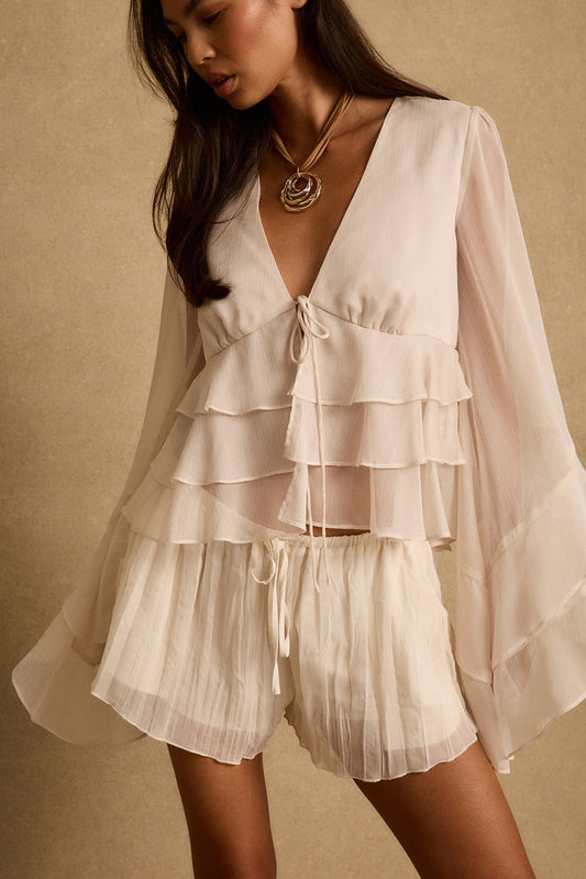 Model wearing the 12th Tribe Alana Cream Blouse, a beautifully lined cream blouse featuring a plunge neckline, functional tie front closure, tiered ruffles, and sheer tulip sleeves. Perfect for vacation maxi skirt pairings, summer brunch looks, and warm weather nights out on the town.