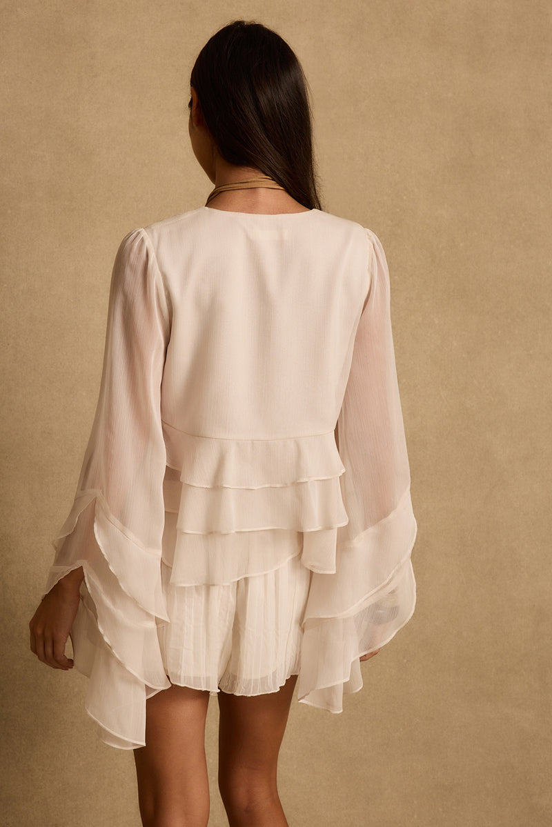 Back view of cream tiered ruffle blouse with tulip bell sleeves on a model.