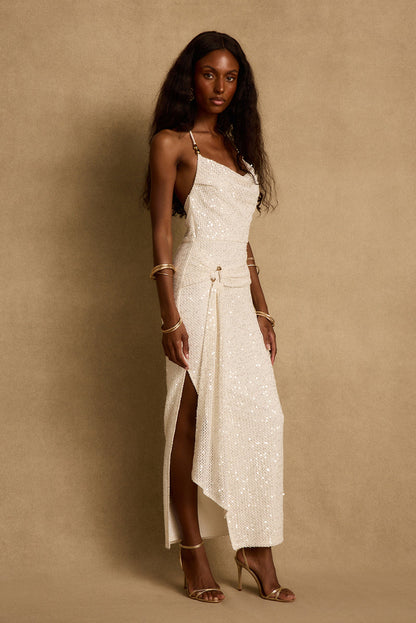 Cream sequin maxi dress with cowl neckline and side leg slit, styled with gold heels.