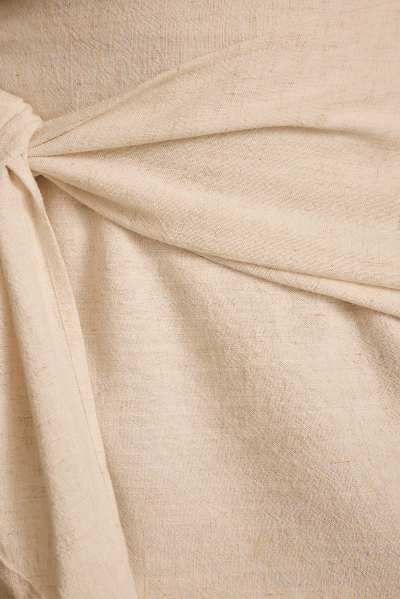 Close-up of natural linen mini skirt showing the relaxed front tie knot detail.