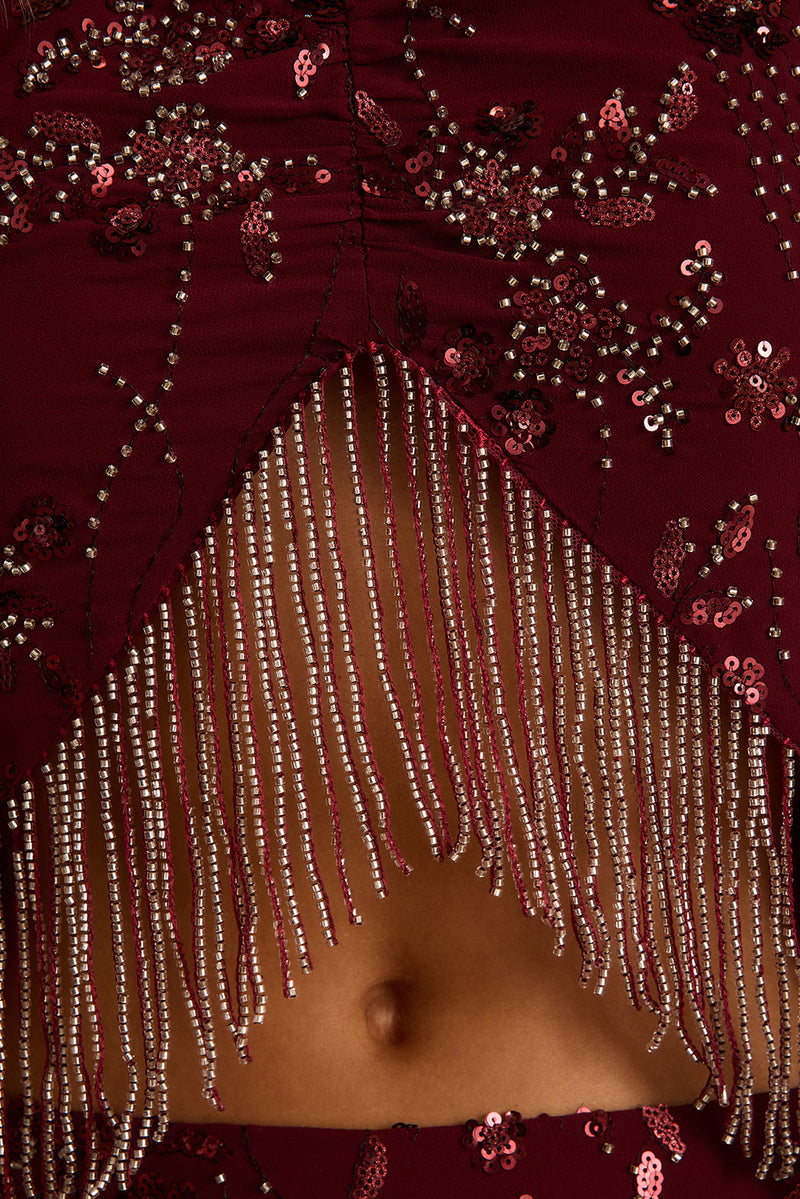 Close-up of mulberry beaded halter top with silver fringe hem and sequin floral detail.