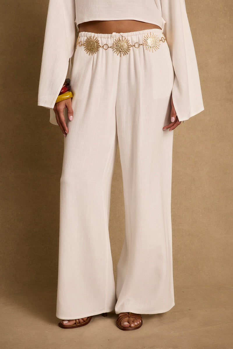 White linen wide-leg pants styled with a gold sun chain belt and sandals.