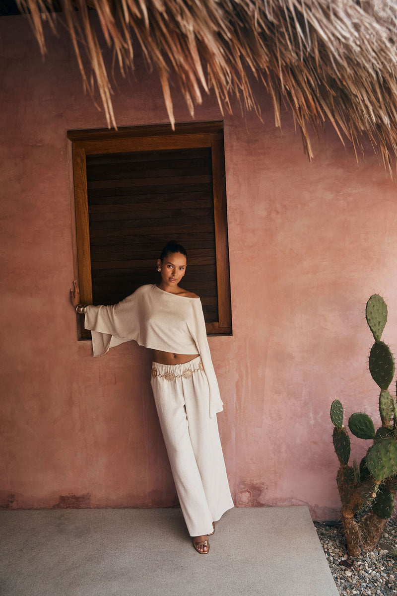 Wide-leg white linen pants styled with a cream top against a sun-warmed terracotta wall.