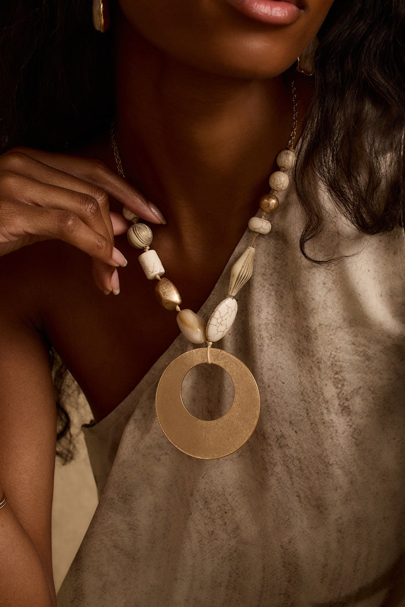 Coral and gold beaded statement necklace with large open circle pendant worn on-model.