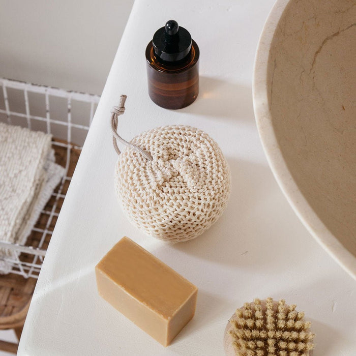 Bath products including a bar of soap, loofah, and bottle on a white surface.