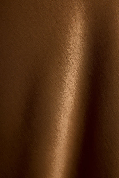Glossy bronze satin fabric of the Dolce maxi dress in a close-up texture detail.