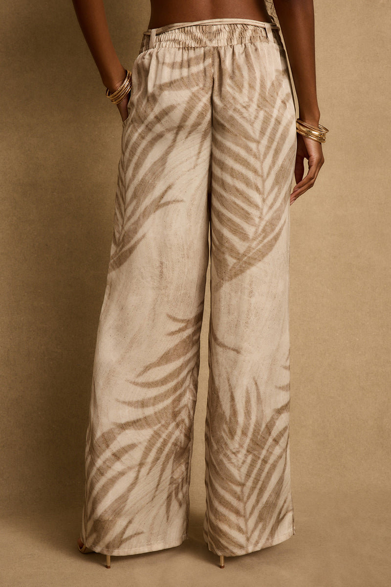 Back view of neutral palm print wide-leg pants with elastic waist and gold bangles.
