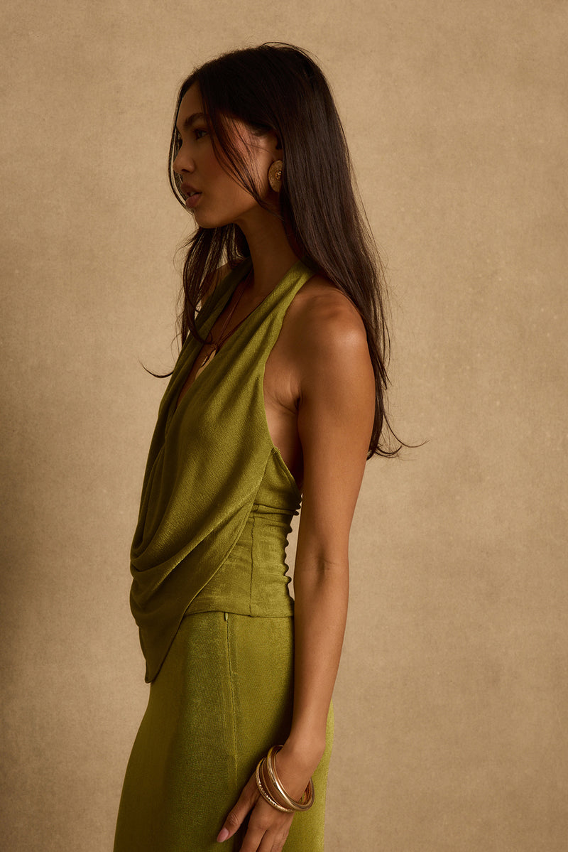 Side profile of model in chartreuse green halter top with draped front and matching skirt.