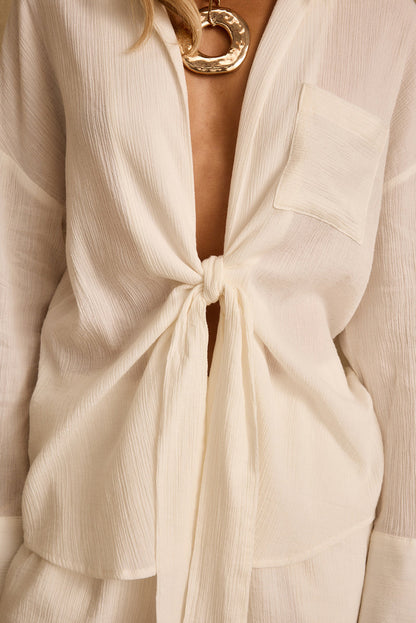 Close-up of ivory gauze tie-front top knotted at the waist with chest pocket.