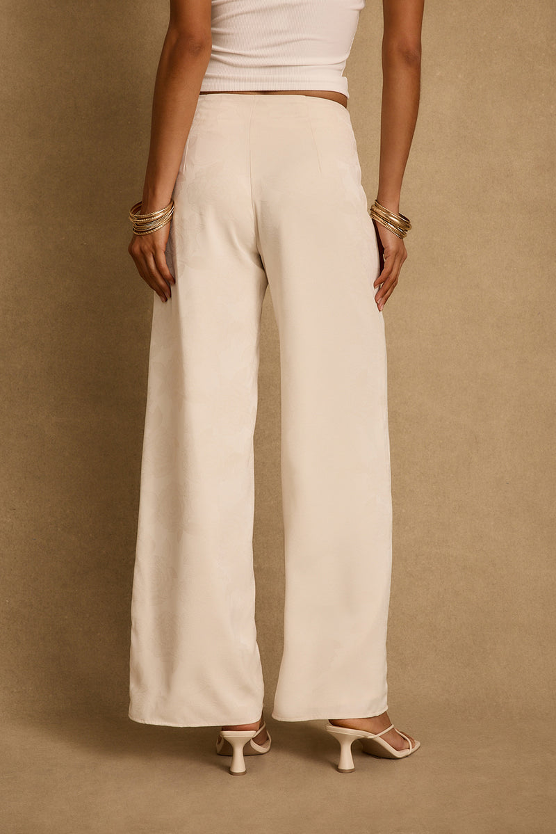 Back view of ivory floral jacquard wide-leg trousers styled with heeled sandals and gold bangles.
