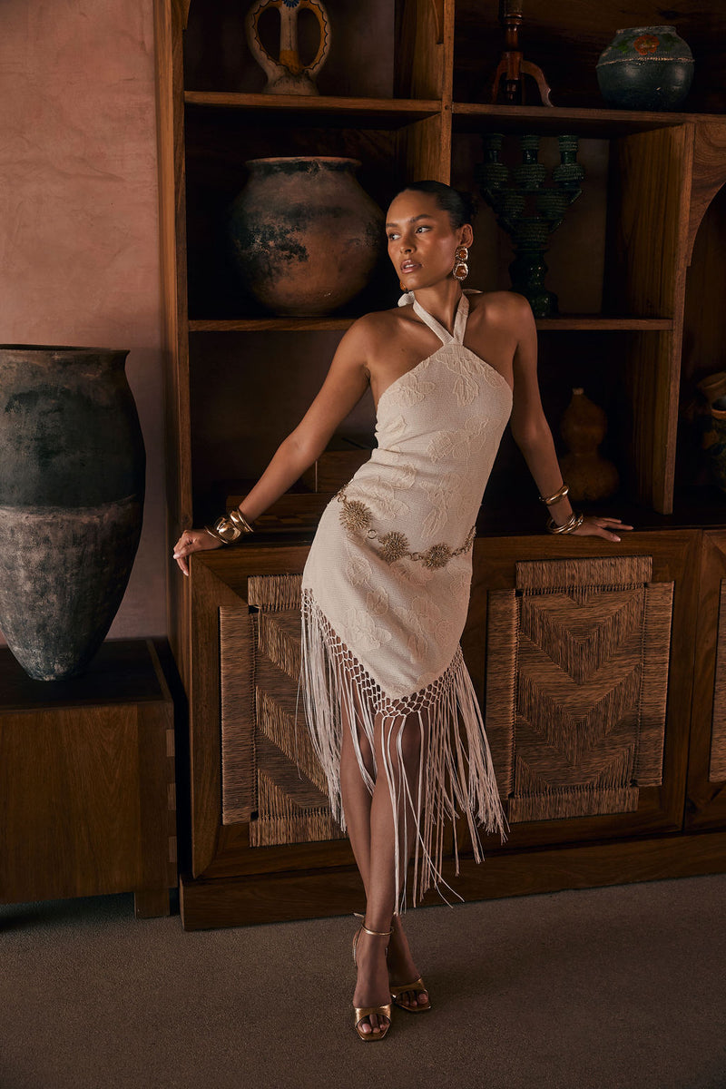 Model wearing the 12th Tribe Fontaine Ivory Jacquard Fringe Midi Dress, an ivory jacquard midi dress featuring a halter tie-back, long fringe hemline, side zipper closure, and woven fabric, perfect for summer soirées, festival-ready looks, vacations with the girls, and stylish warm-weather events