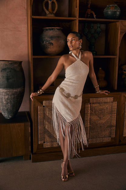 Model wearing the 12th Tribe Fontaine Ivory Jacquard Fringe Midi Dress, an ivory jacquard midi dress featuring a halter tie-back, long fringe hemline, side zipper closure, and woven fabric, perfect for summer soirées, festival-ready looks, vacations with the girls, and stylish warm-weather events