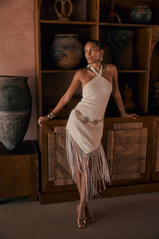 Model wearing the 12th Tribe Fontaine Ivory Jacquard Fringe Midi Dress, an ivory jacquard midi dress featuring a halter tie-back, long fringe hemline, side zipper closure, and woven fabric, perfect for summer soirées, festival-ready looks, vacations with the girls, and stylish warm-weather events