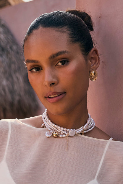 Layered pearl and gold choker worn on-model with gold statement earrings, sheer neckline.