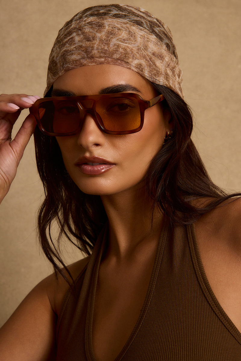 Tortoise shell aviator sunglasses with amber lenses, worn with a leopard-print headscarf.
