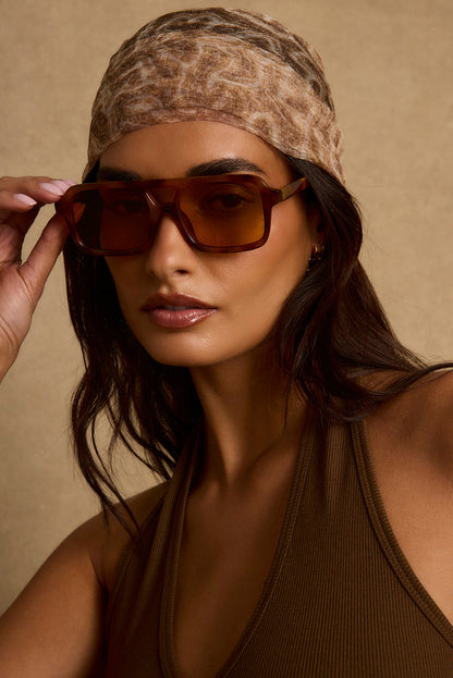 Tortoise shell aviator sunglasses with amber lenses, worn with a leopard-print headscarf.