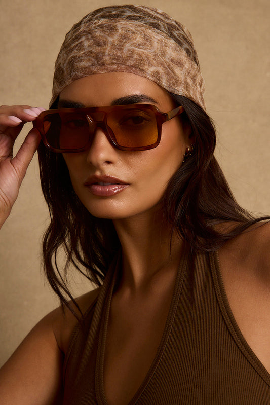 Tortoise shell aviator sunglasses with amber lenses, worn with a leopard-print headscarf.