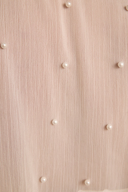 Ivory pearls scattered across sheer blush textured fabric of a pearl-embellished cape.