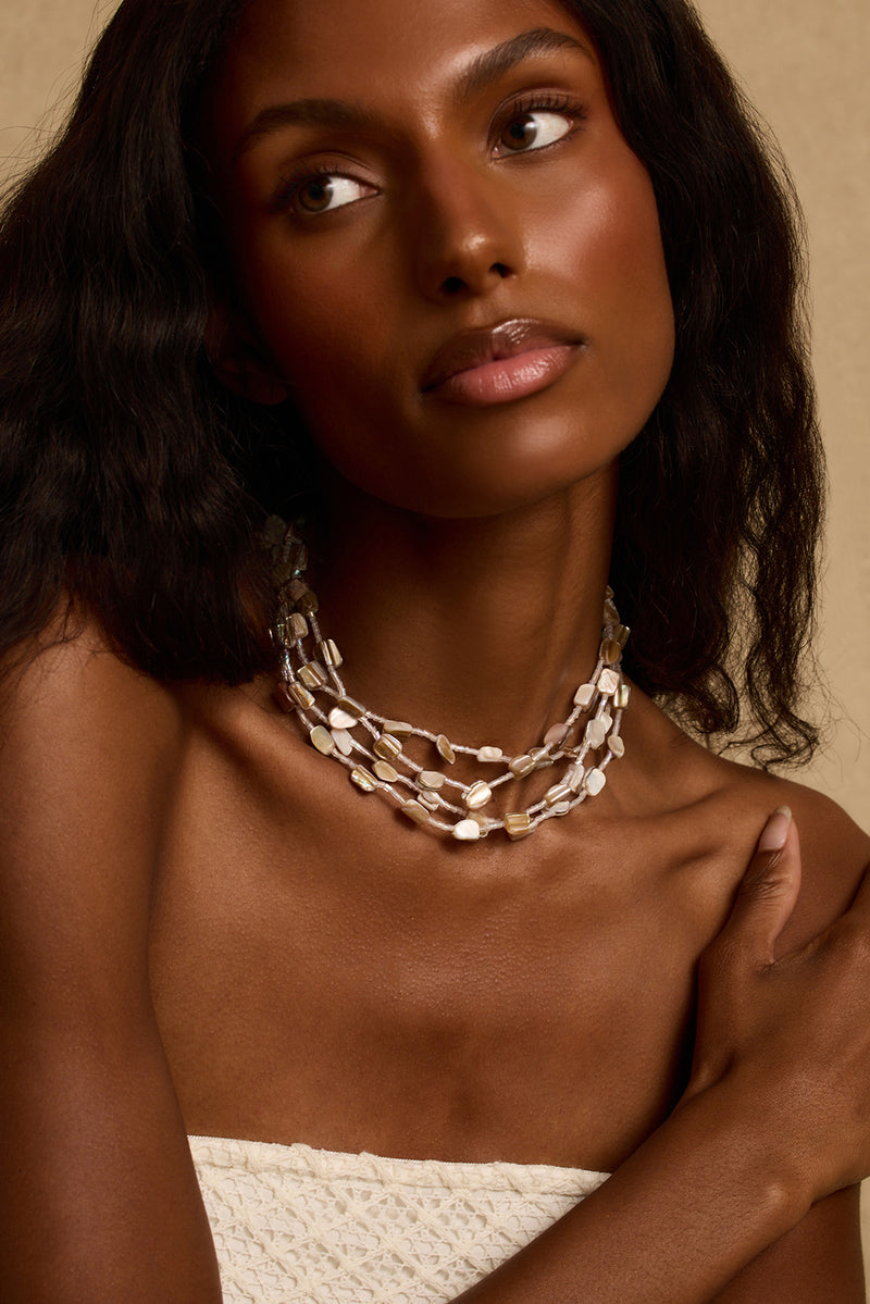 Model wearing the 12th Tribe Kailua Shell Stacked Necklace, a boho-inspired ocean-inspired multi-string shell stacked necklace with a lobster claw clasp closure. Perfect for accessorizing your favorite vacation maxi dress, beach vacation outfit, or summer festival look.