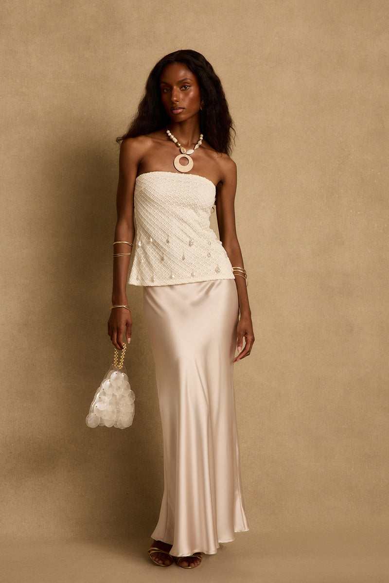 Model wearing the 12th Tribe Laguna Pearl Strapless Top, a stunning lined strapless top featuring dancing pearls and silver bead details, a fishnet overlay, and an easy slip-on style. Perfect for tropical vacation outfits, resort wear looks, and warm weather nights out.