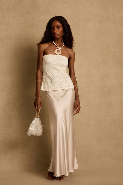 Model wearing the 12th Tribe Laguna Pearl Strapless Top, a stunning lined strapless top featuring dancing pearls and silver bead details, a fishnet overlay, and an easy slip-on style. Perfect for tropical vacation outfits, resort wear looks, and warm weather nights out.