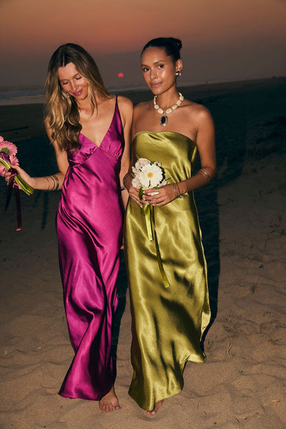 Fuchsia satin maxi dress with plunging V-neckline worn on a beach at sunset.