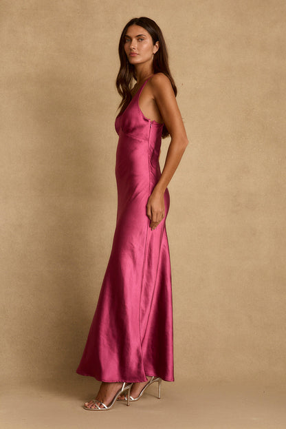 Side profile of the Mirabella fuchsia satin maxi dress styled with metallic strappy heels.