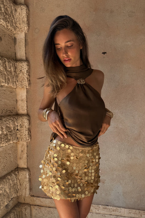 Model wearing the 12th Tribe Miramar Gold Payette Mini Skirt, a best-selling fully lined gold payette mini skirt featuring a low rise fit and a subtle stretch for an ultra-glamorous, comfortable wear. Perfect for summer nights out, rooftop parties, and unforgettable vacation looks.