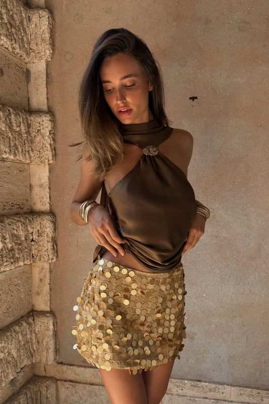 Model wearing the 12th Tribe Miramar Gold Payette Mini Skirt, a best-selling fully lined gold payette mini skirt featuring a low rise fit and a subtle stretch for an ultra-glamorous, comfortable wear. Perfect for summer nights out, rooftop parties, and unforgettable vacation looks.