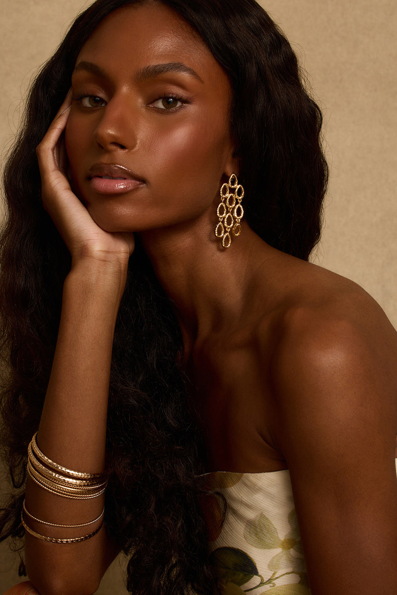 Model wearing the 12th Tribe Paula Gold Statement Earrings, a bold gold circle drop earring with a push back closure for a chic, eye-catching finish. Perfect for pairing with your favorite vacation maxi dress, resort wear looks, and summer nights out.