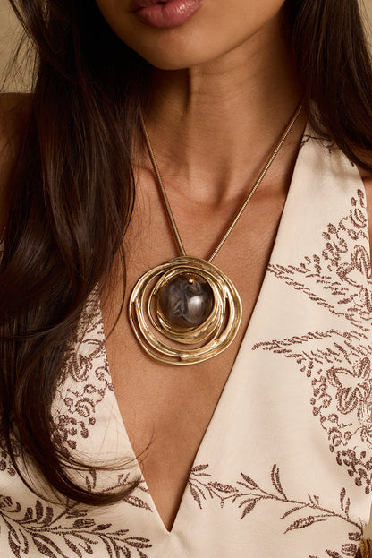 Model wearing the 12th Tribe Queta Gold and Stone Pendant Necklace, a stunning gold chain necklace featuring a stone and gold pendant centerpiece with a lobster claw closure. Perfect for accessorizing your favorite vacation maxi dress, beach vacation outfit, or summer evening look.