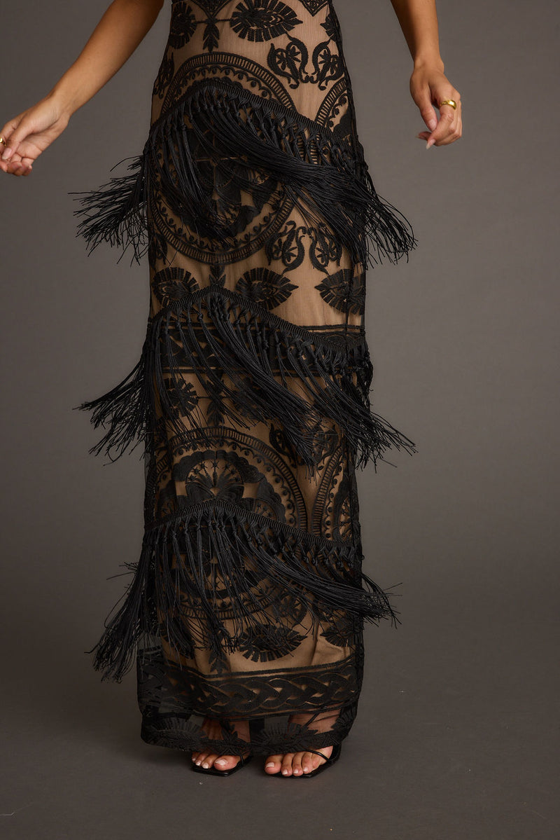 Detail of black lace fringe maxi dress skirt over nude mesh, with tiered fringe.