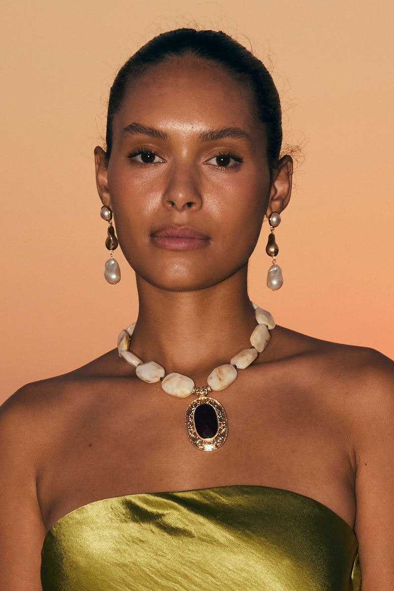 Model in green satin top wearing a beaded stone statement pendant necklace and pearl earrings.
