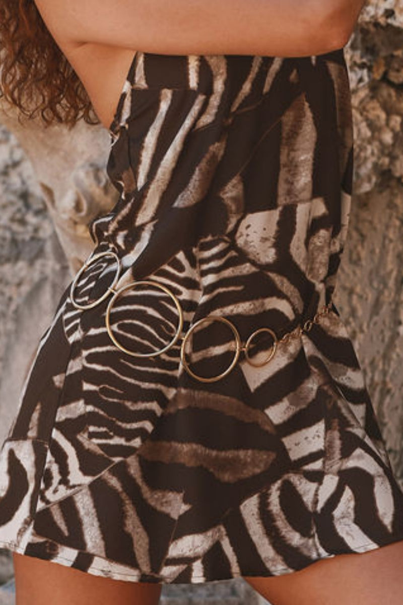Gold circle-link chain belt worn over a zebra-print resort dress.