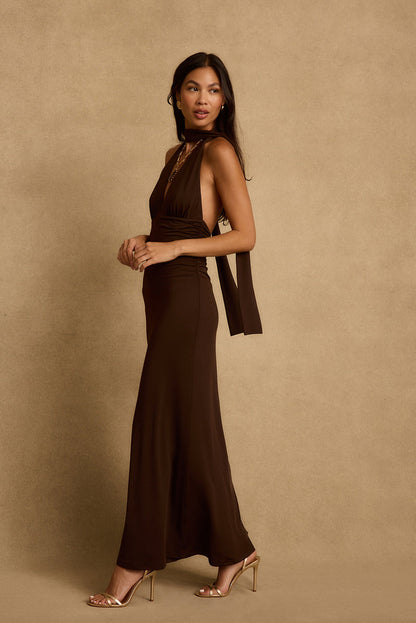 Side view of the Valencia brown maxi dress with scarf neck tie and gold heels.