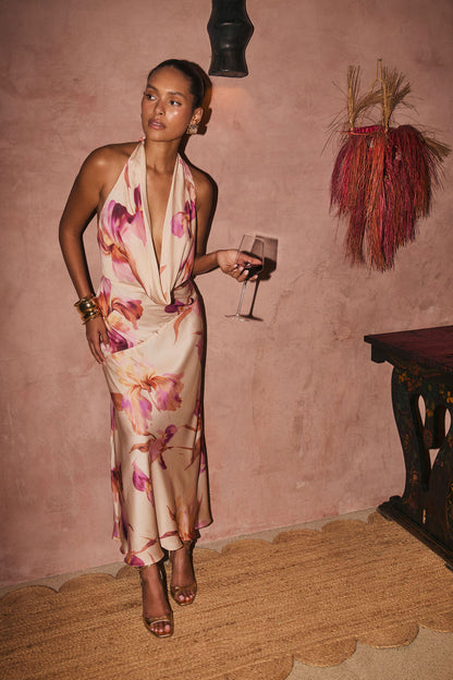 Model wearing the 12th Tribe Valentina Light Pink Floral Maxi Dress, a satin floral maxi dress featuring a deep cowl neckline, bias-cut skirt, halter tie-back, and lace-up back with zipper closure, perfect for summer soirées, vacation looks, and elegant warm-weather events