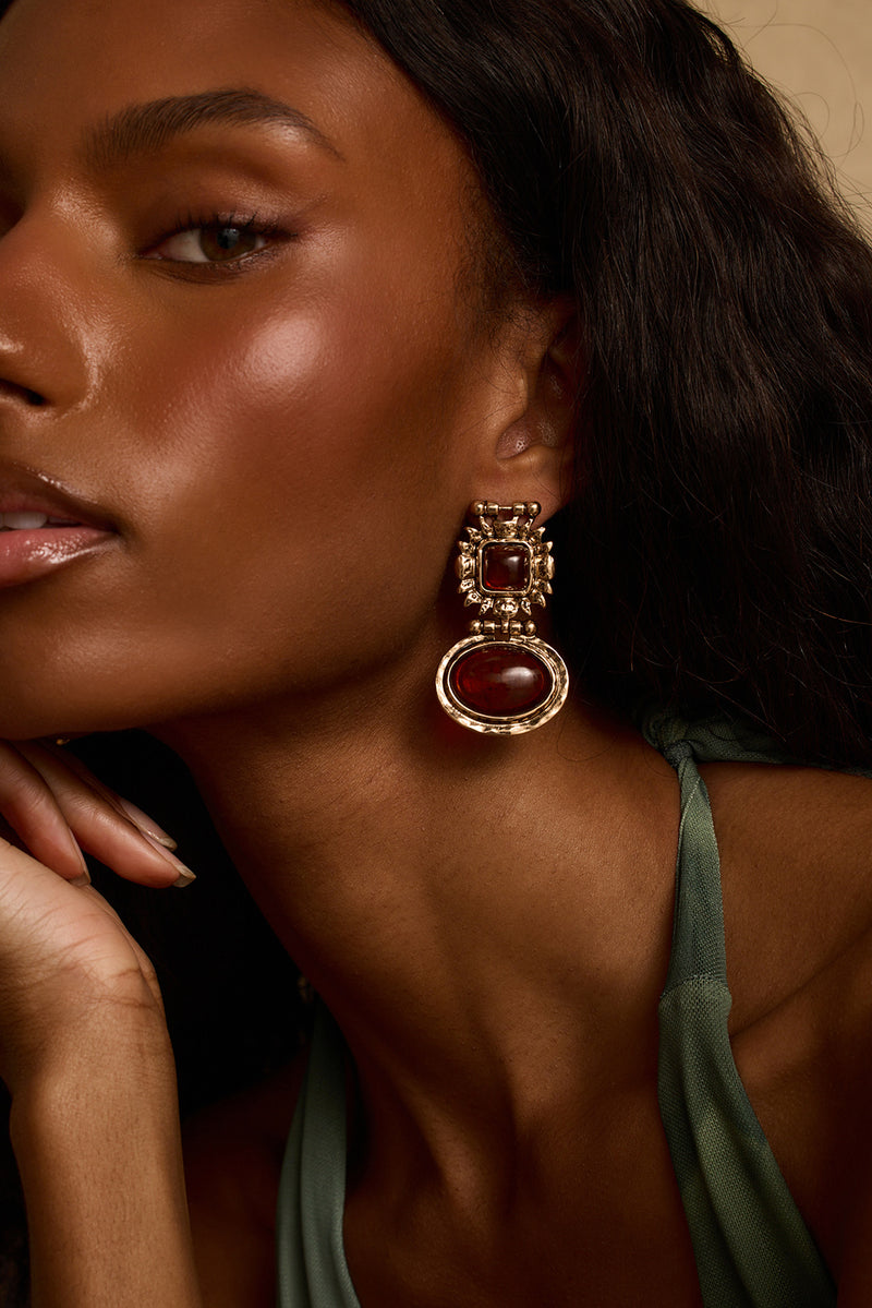 Model wearing the 12th Tribe Villa Amber Earrings, stunning amber and gold chunky stone drop earrings featuring a push back closure for a bold, statement-making finish. Perfect for pairing with your favorite vacation maxi skirt, resort wear look, or summer nights out.