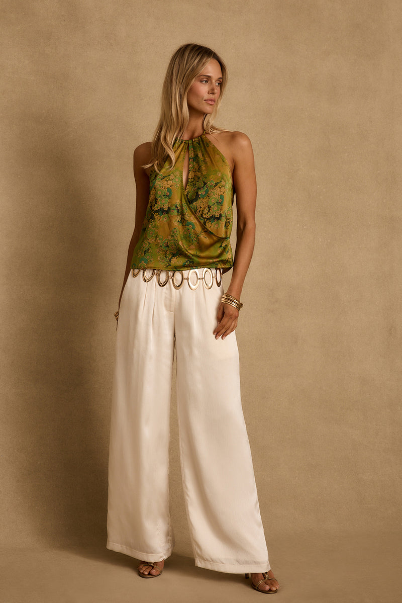 Model wearing the 12th Tribe Wild Hibiscus Chartreuse Halter Top in vibrant Spring ready gold and green pattern. Featuring a halter neckline and cropped fit. Style with high-waisted bottoms for festivals, bachelorette parties, and statement summer looks.