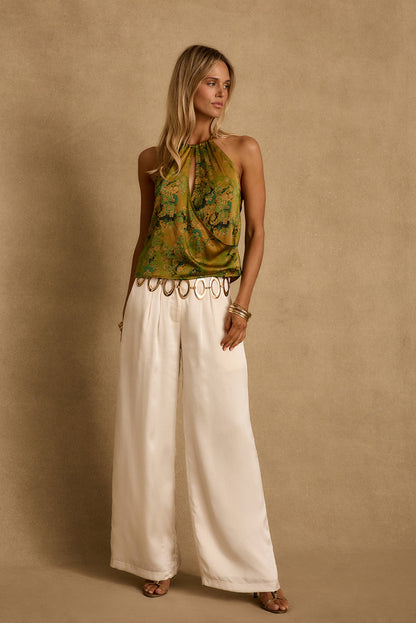 Model wearing the 12th Tribe Wild Hibiscus Chartreuse Halter Top in vibrant Spring ready gold and green pattern. Featuring a halter neckline and cropped fit. Style with high-waisted bottoms for festivals, bachelorette parties, and statement summer looks.