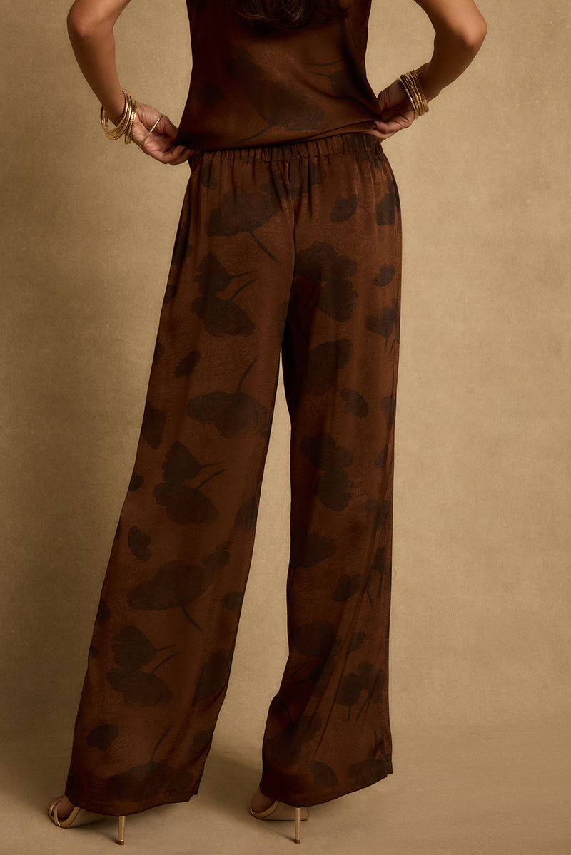 Back view of espresso brown floral satin pants with elastic waist and wide legs.